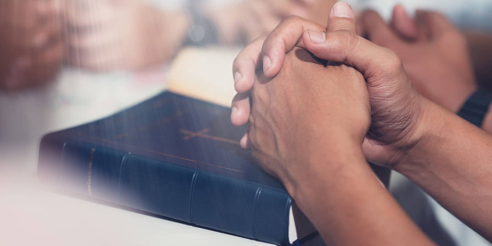 Close up of a persons hands folded in prayer on their Bible.