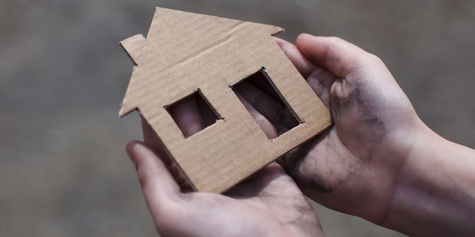 A close-up of a person holding a cut-out cardboard house in their hands