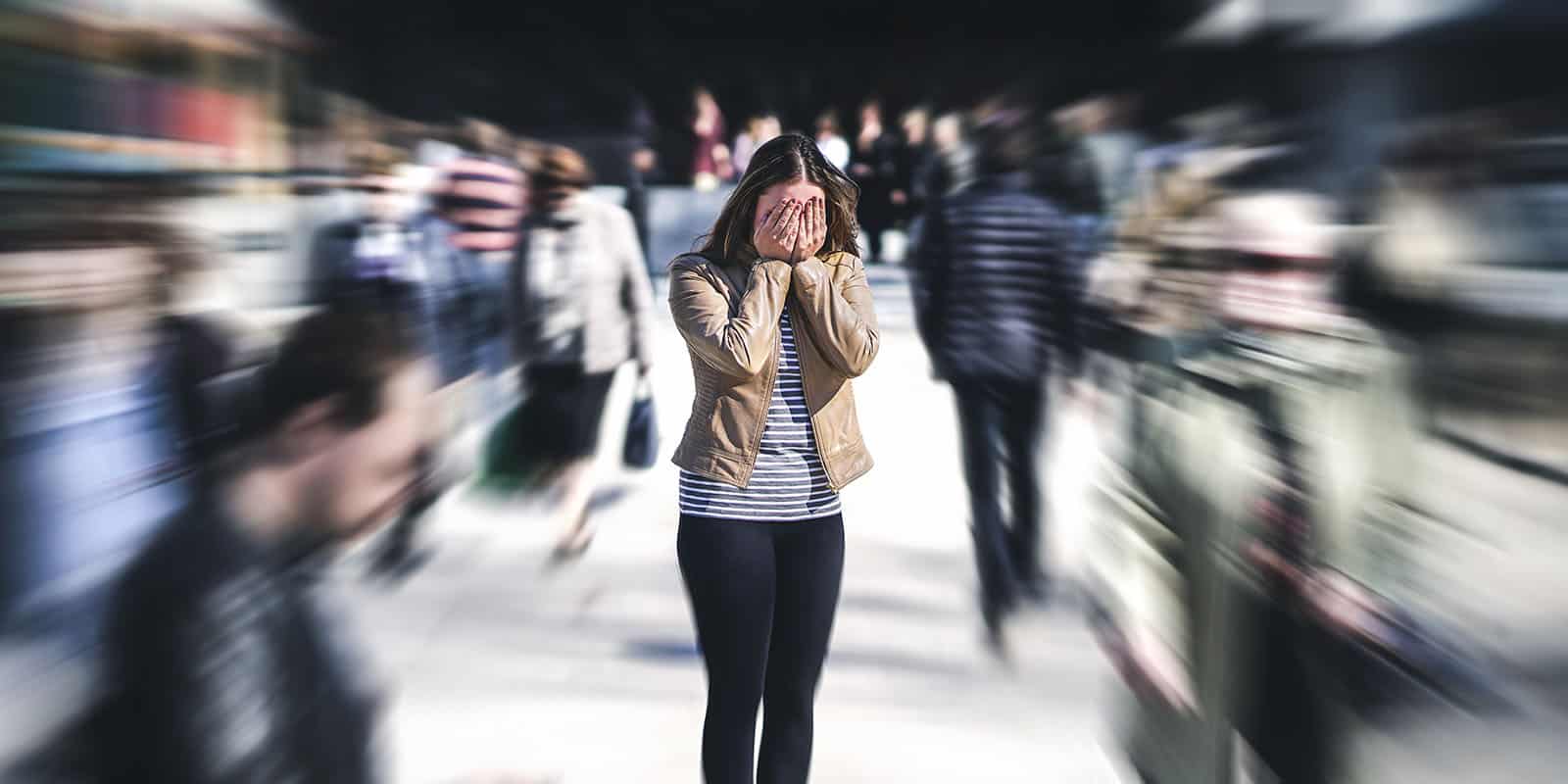 Woman standing in a crowd of people overwhelmed and covering her face